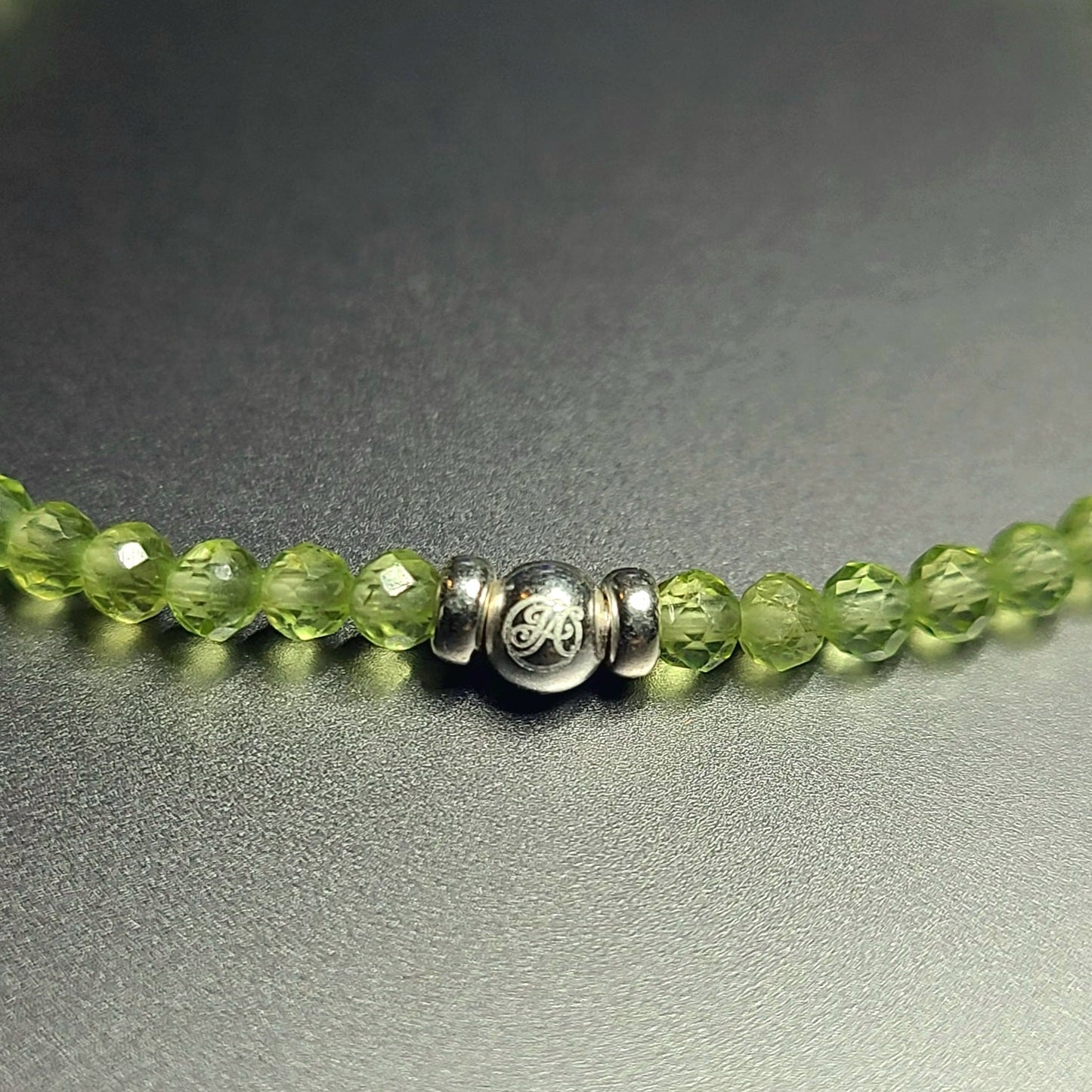 Close-up of the sterling silver John Alex signature bead with 3 mm faceted peridot beads